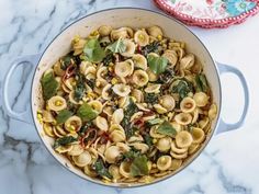 a pot filled with pasta and spinach on top of a marble counter next to a plate