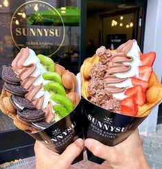 two people holding up ice creams in front of a store window with fruit and cookies