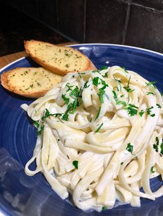 a blue plate topped with pasta next to two slices of bread on top of a wooden table