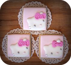 three decorated cookies in the shape of hello kitty on a lace doily with pink bows