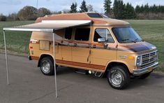 an orange and brown van parked on the side of a road next to a field