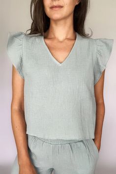 A woman modeling a sea blue cotton gauze ruffled sleeve top with matching pants Cotton Flutter Sleeve Top For Brunch, Cotton Tops With Ruffle Sleeves For Daywear, Cotton Blouse With Flutter Sleeve And Relaxed Fit, Cotton Blouse With Relaxed Fit And Flutter Sleeves, Relaxed Fit Cotton Blouse With Flutter Sleeves, Relaxed Fit Cotton Blouse With Ruffle Sleeves, Casual Tops With Ruffle Sleeves For Daywear, Trendy Ruffled Tops For Loungewear, Relaxed Fit Ruffle Sleeve Tops For Daywear