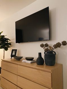 a flat screen tv mounted on the wall above a dresser with vases and books