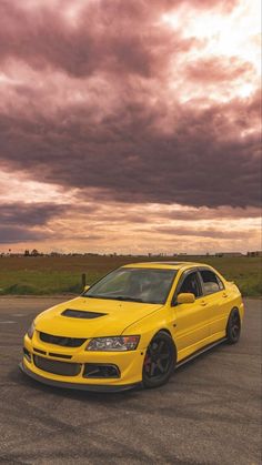 a yellow car parked in a parking lot under a cloudy sky with clouds above it