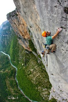 a man climbing up the side of a mountain with his hands in the air while holding onto an orange helmet