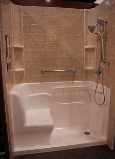 a bathtub in a bathroom with tiled walls and flooring on the wall, next to a shower head