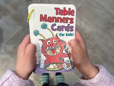 a person holding up a book in front of their face with the title table mannerss cards for kids