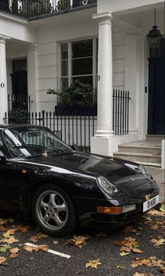 a black sports car parked in front of a white house with columns and railings