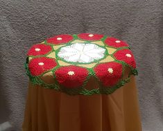 a red and green crocheted table cloth on top of a round tablecloth