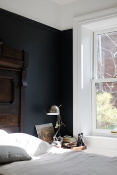 a bed with white sheets and pillows in front of a window next to a lamp