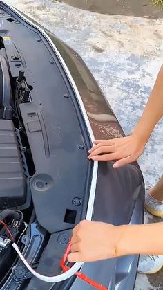 a woman is working on the hood of a car with an electric wire connected to it