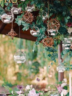 the table is set with flowers, candles and hanging glass globes on it's branches