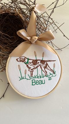 a bird nest with two birds and the words beau on it, hanging from a ribbon