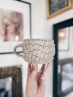 a hand holding up a ceramic cup with black dots on it's sides and eyes