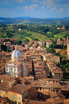 an aerial view of a city with many buildings and green hills in the background,