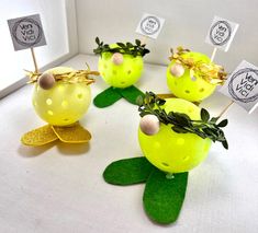 four yellow plastic apples with green leaves and decorations on them, sitting in front of a window