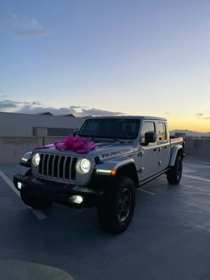 a silver jeep with a pink bow on it's hood parked in a parking lot