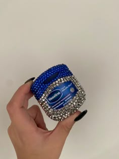 a hand holding a blue and silver beaded ring with black nail polish on it