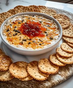 a bowl of dip surrounded by crackers on a platter with cheese and sauce