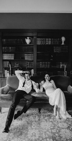 a man and woman sitting on a couch in front of a book shelf filled with books