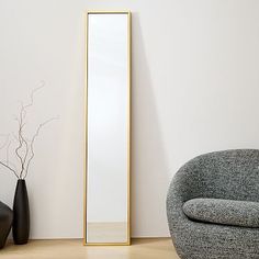 a large mirror sitting next to a chair and vase on the floor in front of a white wall