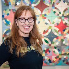 a woman wearing glasses standing in front of a wall with colorful circles on it's sides