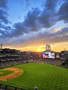 a baseball stadium filled with lots of people watching the sun go down over the field