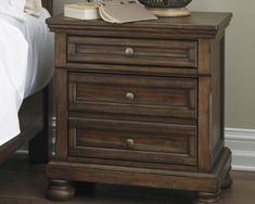 a night stand with an open book on it and a vase sitting on top of it