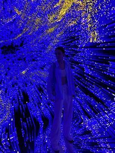 a woman standing in front of a blue wall with lights on it and an abstract pattern behind her