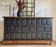 a black dresser with many drawers on top of it next to a mirror and vase