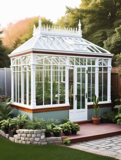 a small white greenhouse in the middle of a yard with potted plants and trees