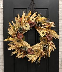 a wreath is hanging on the front door with pine cones and other autumn decorations around it