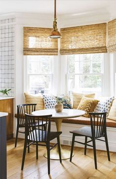 a kitchen table with chairs and a bench in front of a window that has roman shades on the windowsill