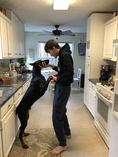 a man standing next to a dog in a kitchen on top of a floor rug