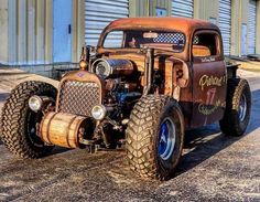 an old model truck with large tires parked in front of a garage door on the street