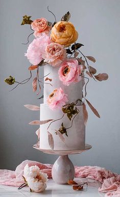 a three tiered white cake with pink and yellow flowers on top, sitting on a table