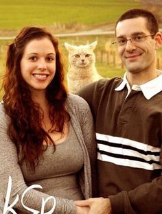 a man and woman standing next to each other with a cat on their shoulder in front of them