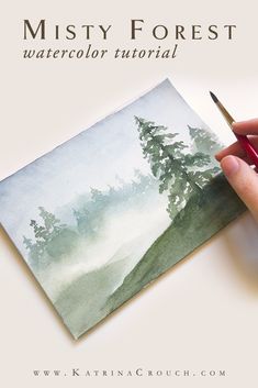 a person is holding a pen and drawing a landscape with watercolor paint on paper