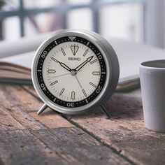 an alarm clock sitting on top of a wooden table next to a book and cup