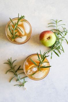 three glasses filled with drinks and garnished with rosemary sprigs next to an apple