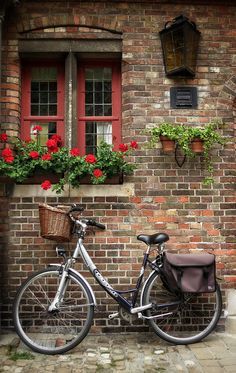 a bicycle parked in front of a brick building with red flowers on the windowsill