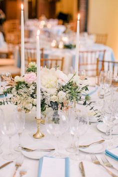 the centerpieces on this table are white and pink flowers, greenery, and candles