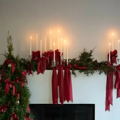 a fireplace decorated for christmas with candles and red bows on the mantel above it