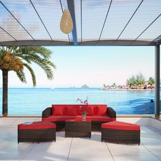 an outdoor living area with red couches and palm trees on the water's edge