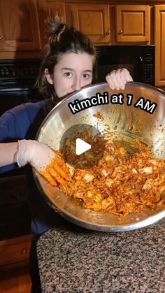 a woman holding up a large metal bowl with food in it and the words kimchi at 1 am