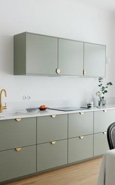 a kitchen with green cabinets and gold handles on the countertop, along with a dining table