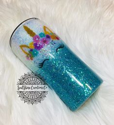 a blue cup with unicorns on it sitting on top of a white fur covered floor