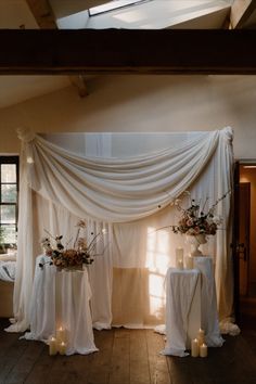 two tables with white linen draped over them and candles in front of the table are decorated with flowers