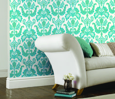 a white couch sitting in front of a wall with green and white designs on it