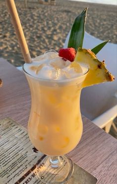 a pineapple drink is sitting on a table at the beach with a straw in it